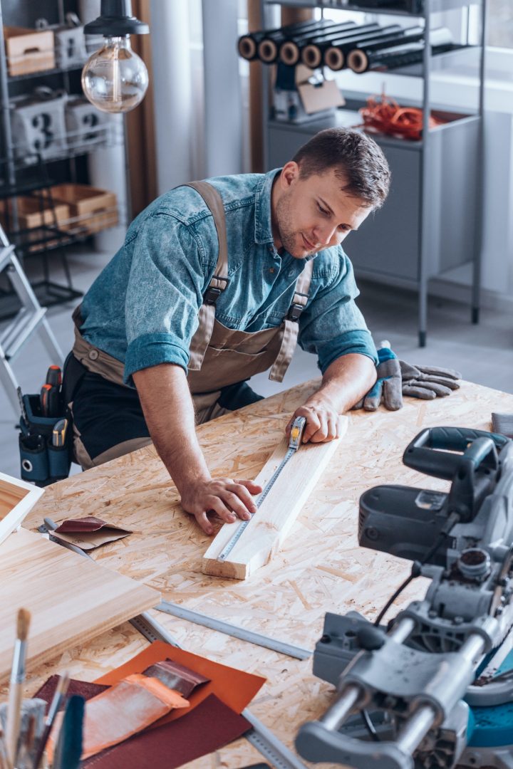 Modern carpenter measuring wooden plank